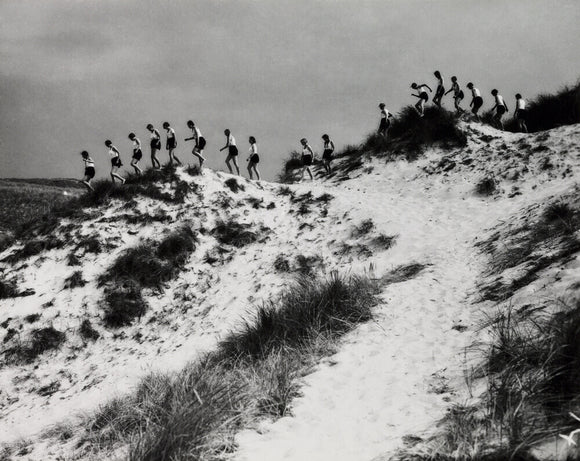Horizon line of women walking over dunes, about 1930.