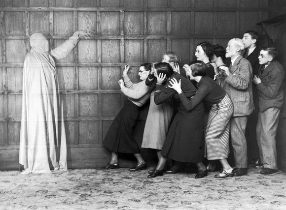 People 'cowering in fear' at the sight of a ghost, c 1920s.