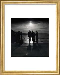 Figures silhouetted by the moon on a promenade, c 1930s.