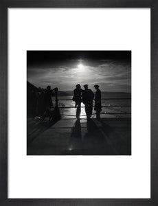 Figures silhouetted by the moon on a promenade, c 1930s.