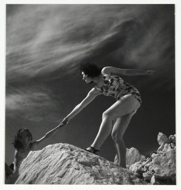 Woman helping child climb onto a rock, about 1935