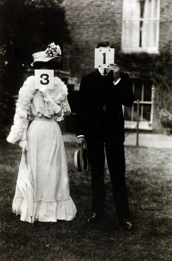 A couple, each holding up a number in front of their face circa 1905